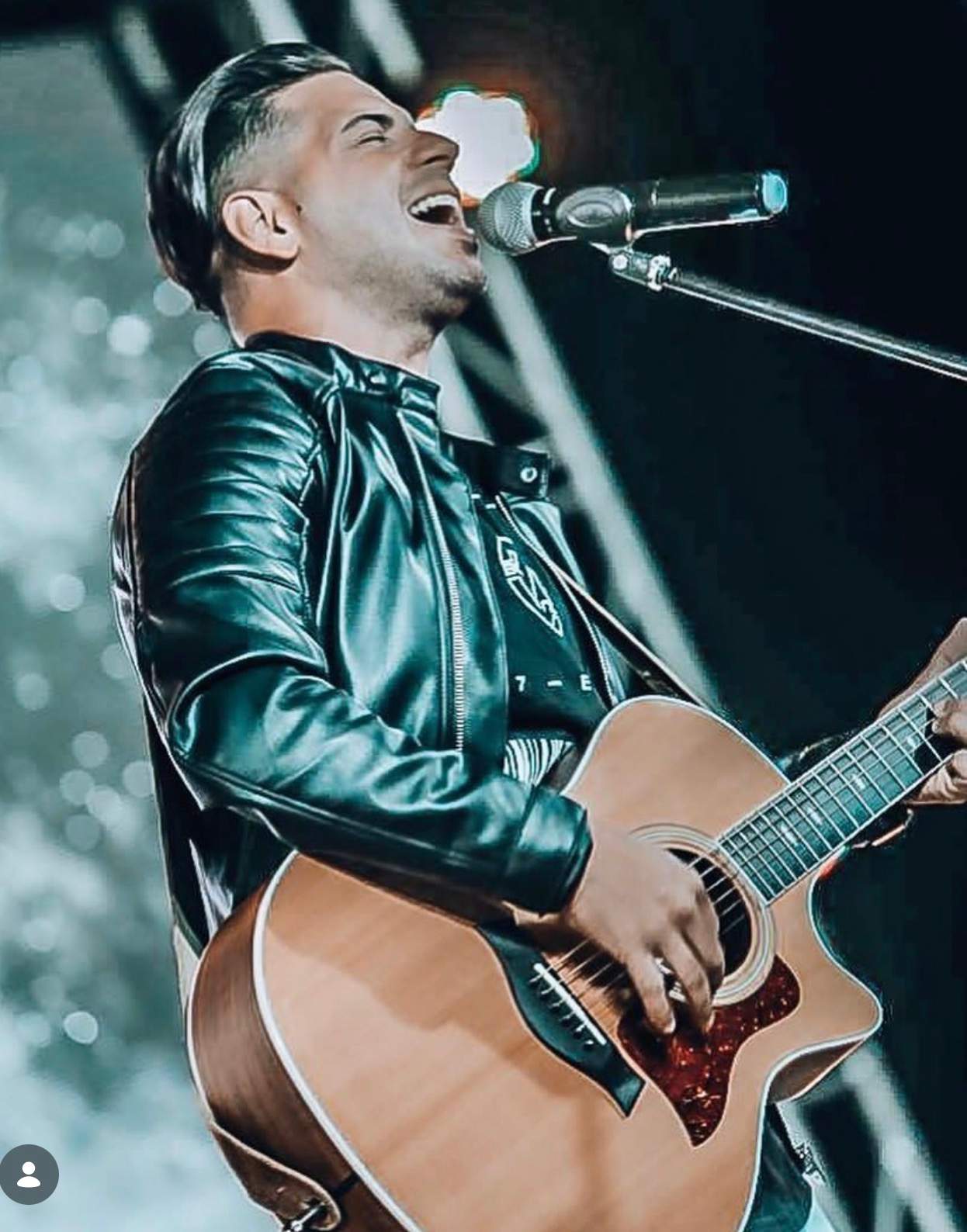 Edgar René cantando con guitarra acústica bajo luces de escenario