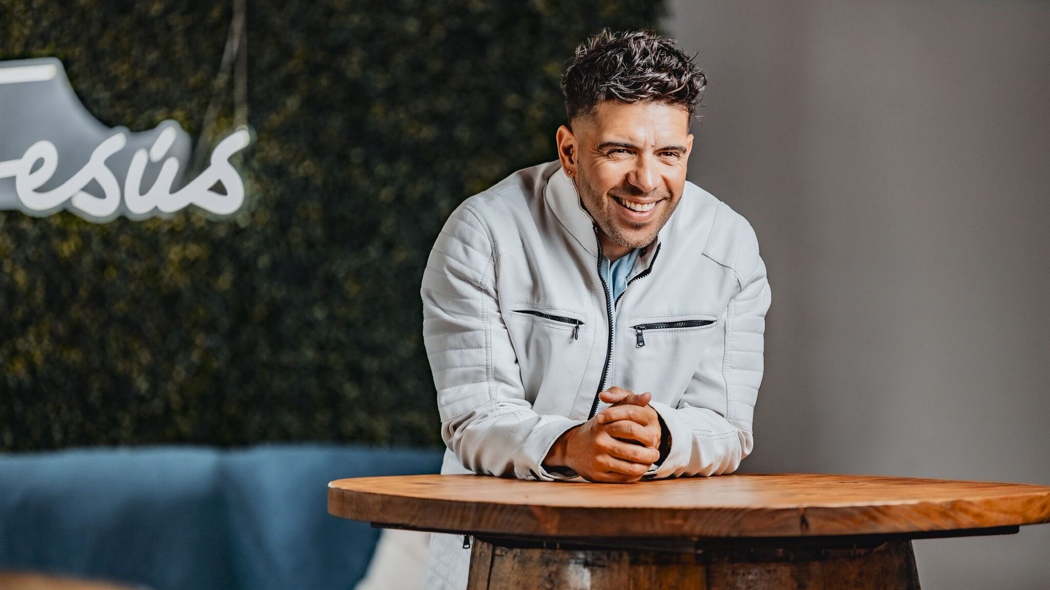 Edgar René sonriendo, apoyado sobre una mesa de madera, con chaqueta blanca