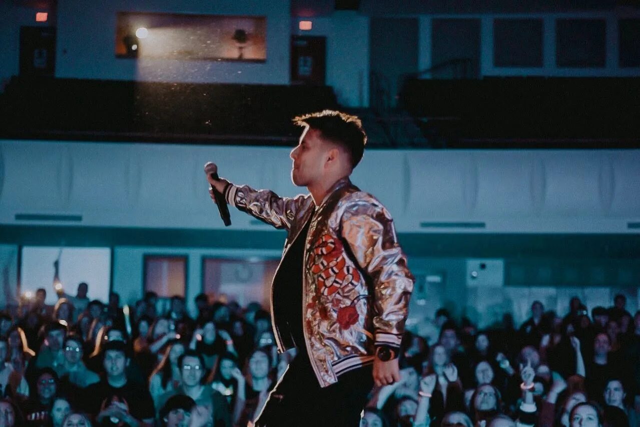 Edgar René cantando en el escenario de un concierto escolar frente a un auditorio lleno de estudiantes
